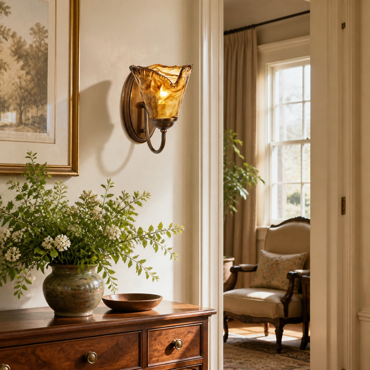 Amberkleurige wandlamp van geribbeld glas naast een schilderij, boven een ladekast met bloemen, met zicht op een zitkamer